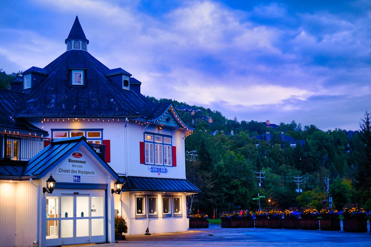 about-01 Beautiful evening view of Chalet des Voyageurs in Mont Tremblant with vibrant skies and lush greenery.