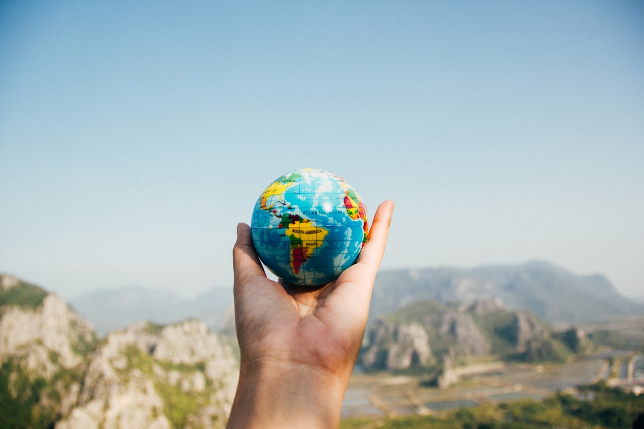 hero-img Hand holding a globe against a mountain background symbolizing travel and exploration.